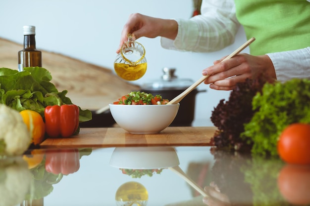 Mains humaines inconnues cuisinant dans la cuisine. La femme est occupée avec une salade de légumes. Repas sain et concept de nourriture végétarienne.