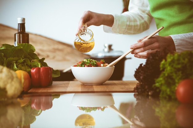 Des mains humaines inconnues cuisinent dans la cuisine. Une femme est occupée à préparer une salade de légumes. Un repas sain et un concept de nourriture végétarienne.