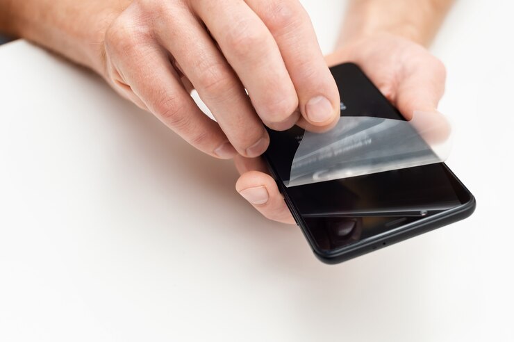 Des mains humaines retirant un film protecteur de l'écran d'un smartphone