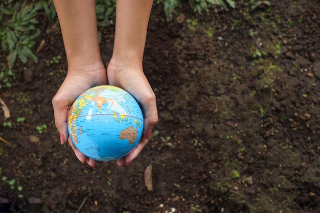 Mains humaines tenant le globe terrestre sur fond de sol. Concept de jour de la terre avec espace de copie.