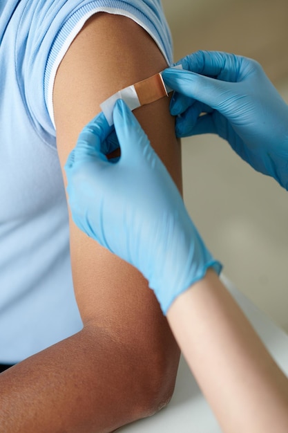 Mains d'une infirmière collant un pansement adhésif sur le site d'injection du vaccin