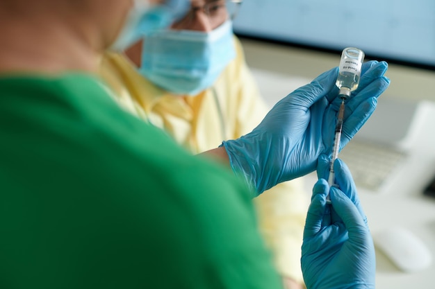 Mains d'une infirmière médicale remplissant une seringue avec un vaccin contre le coronavirus à partir d'un flacon