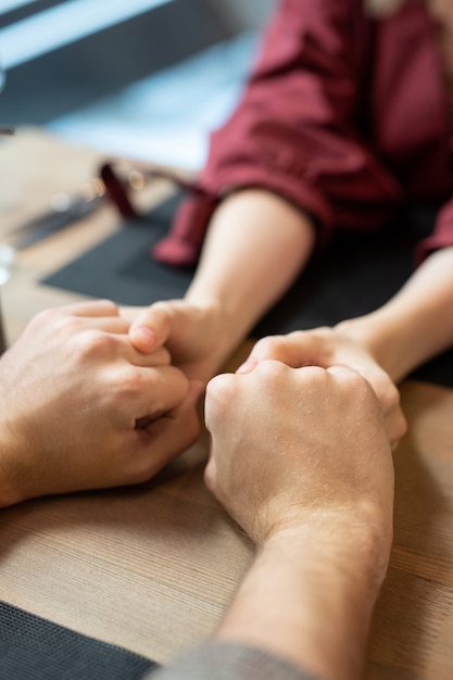 Mains de jeune couple hétérosexuel amoureux et affectueux assis par table servie pendant le dîner dans un restaurant ou un café contemporain