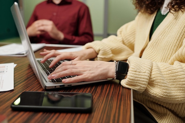 Mains de jeune femme d'affaires touchant les touches du clavier d'ordinateur portable par table