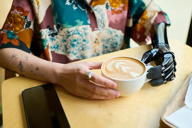 Mains de jeune femme avec bras partiel tenant une tasse de cappuccino