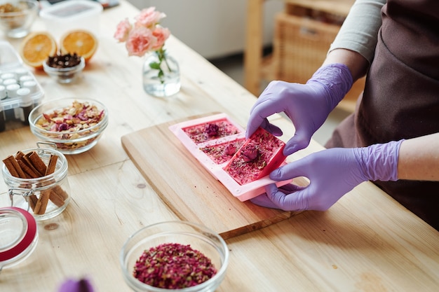 Mains de jeune femme dans des gants en caoutchouc lilas prenant du savon rose fait à la main à partir de moules en silicone