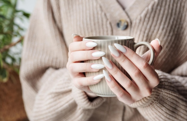 Mains d'une jeune femme avec une manucure blanche sur les ongles