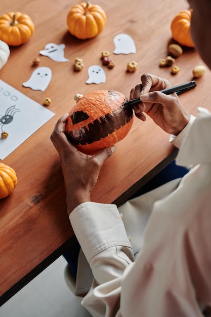 Photo les mains d'une jeune femme méconnaissable dessinant un visage effrayant sur une citrouille d'halloween