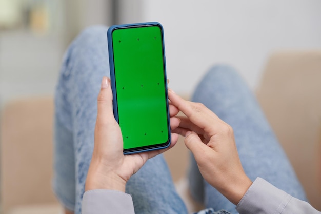 Mains de jeune femme moderne tenant un téléphone portable avec un écran vert vierge