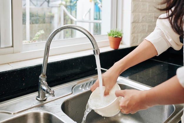 Mains de jeune femme rinçant le bol avec de l'eau du robinet après avoir pris le petit déjeuner à la maison