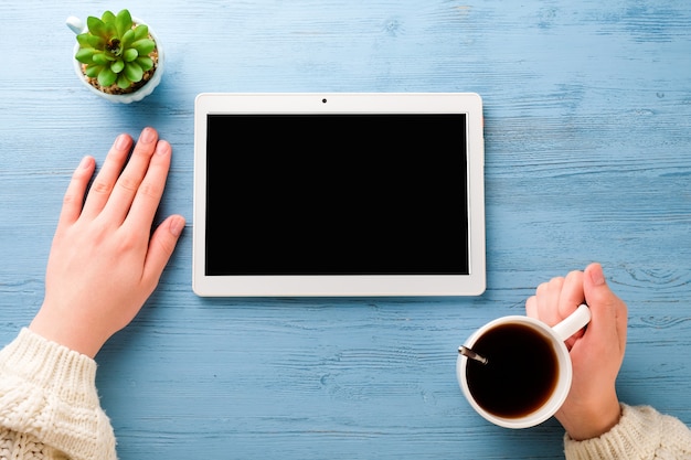 mains d'une jeune femme avec tablette et café sur une table bleue