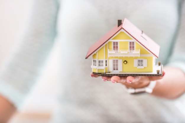 Mains de jeune femme tenant une maison modèle.