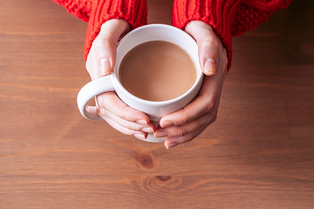 Mains de jeune femme tenant une tasse de café chaud sur un bureau en bois. Copiez l'espace. Vue aérienne. Temps de repos.