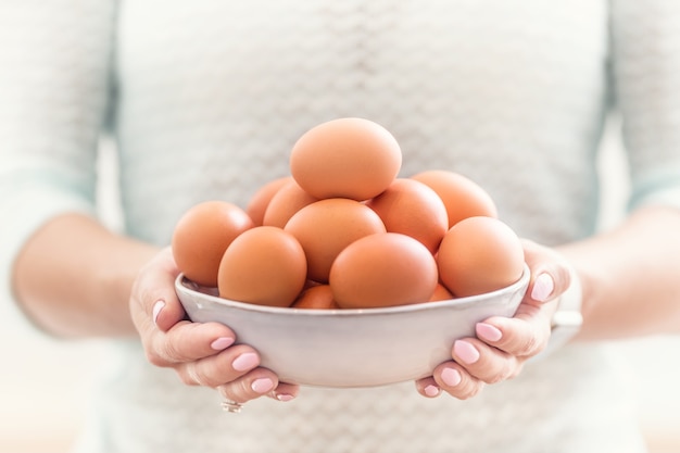 Les mains d'une jeune femme tiennent un bol d'œufs de poule.