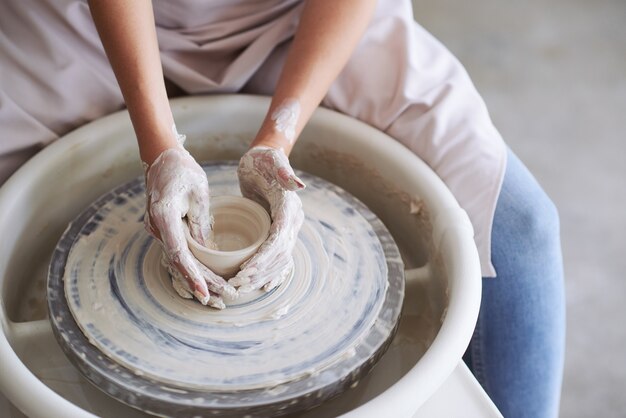 Mains de jeune femme travaillant sur un tour de potier dans un atelier confortable et fabriquant un vase ou une tasse