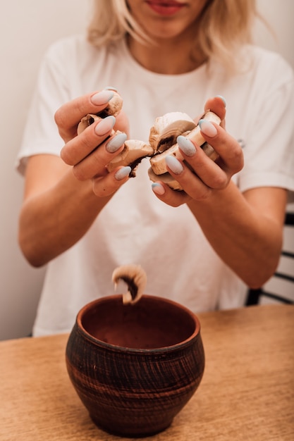 Mains D'une Jeune Femme Versant Des Champignons Hachés Dans Une Casserole Dans La Cuisine