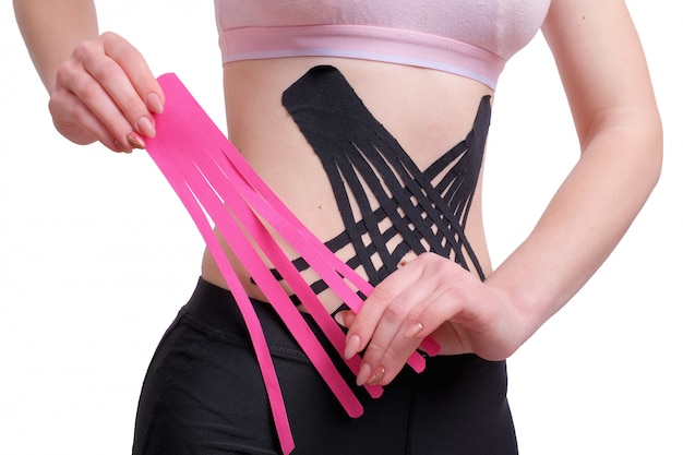 Mains de jeune fille appliquant du ruban rose kinesio sur son abdomen