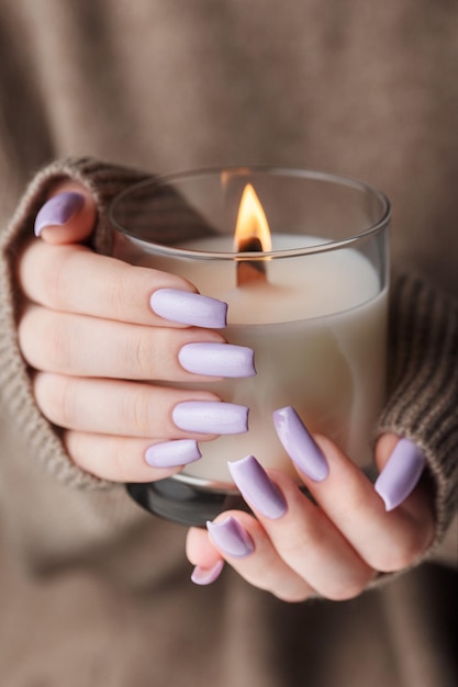 Les mains d'une jeune fille avec une belle manucure violet clair tiennent une bougie