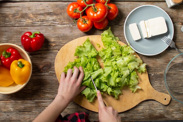 Mains de la jeune fille couper la laitue sur une table, une femme prépare une salade de légumes, des aliments sains, un couteau hache les verts