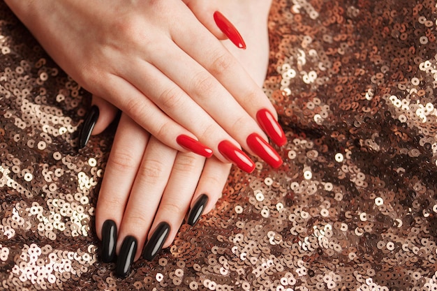 Mains d'une jeune fille avec une manucure rouge et noire sur les ongles