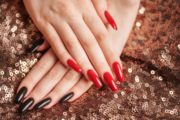 Mains d'une jeune fille avec une manucure rouge et noire sur les ongles