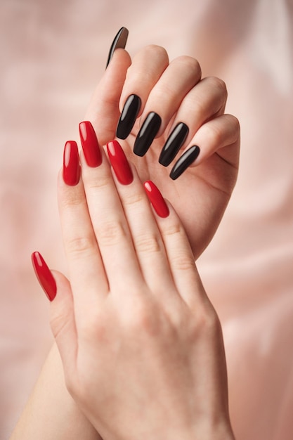 Mains d'une jeune fille avec une manucure rouge et noire sur les ongles