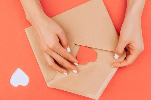 Les mains de la jeune fille mettent un cœur découpé sur le fond dans une enveloppe. Carte de la Saint-Valentin. Concept de la Saint-Valentin. Mise à plat.