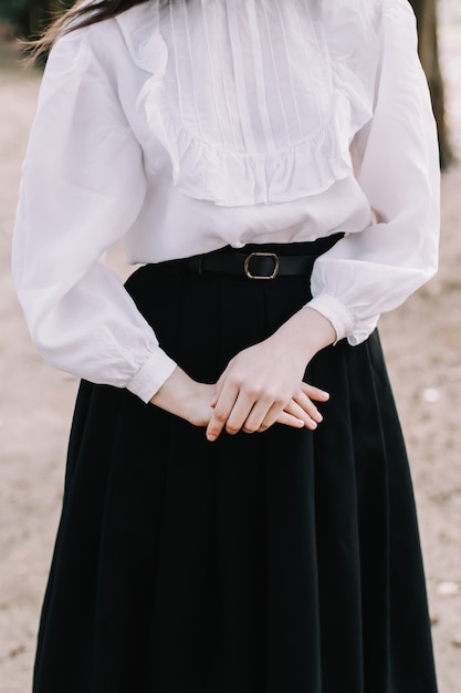 Mains d'une jeune fille portant une jupe noire et un chemisier blanc vintage