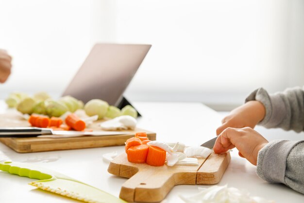 Les mains d'une jeune fille préparant la nourriture dans la cuisine avec une tablette en arrière-plan