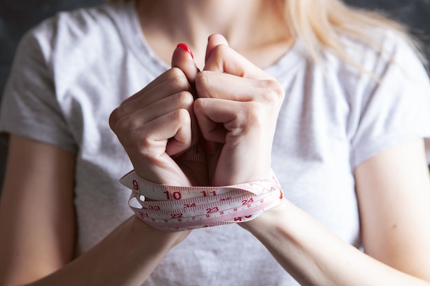 Les mains d'une jeune fille sont attachées avec un ruban à mesurer