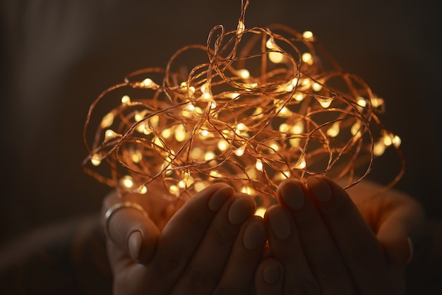 Mains d'une jeune fille tenant une guirlande de lumières de Noël sur un fond sombre