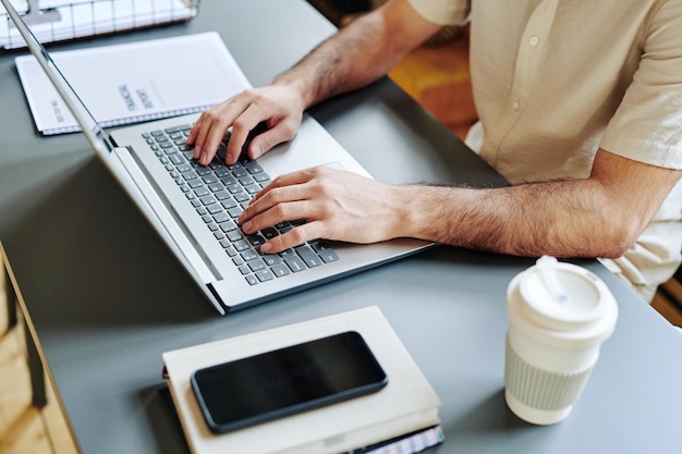 Mains d'un jeune homme d'affaires tapant sur un clavier d'ordinateur portable près de son lieu de travail