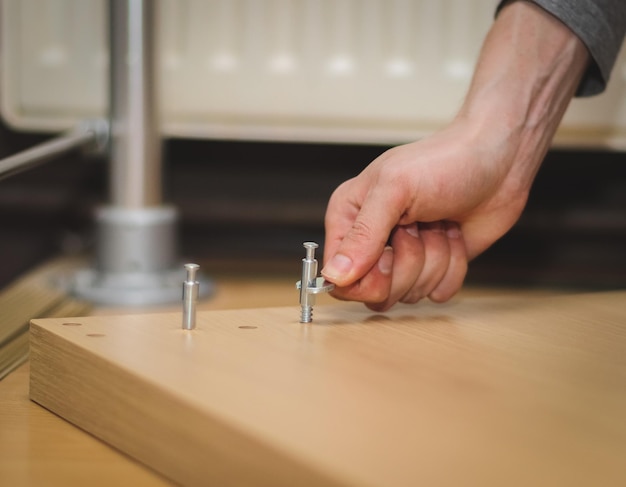 Les mains d'un jeune homme caucasien avec une clé serrent un boulon sur la partie en bois du lit