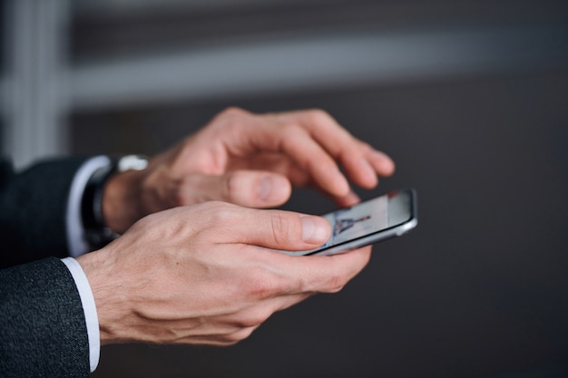 Mains de jeune homme élégant en tenue de soirée à l'aide de smartphone pour regarder des photos ou les publier sur les réseaux sociaux