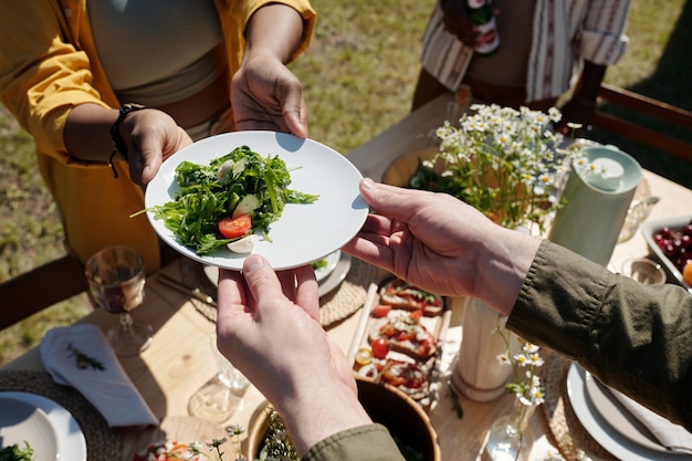 Mains de jeune homme prenant une assiette avec une salade de légumes passée par une femme noire