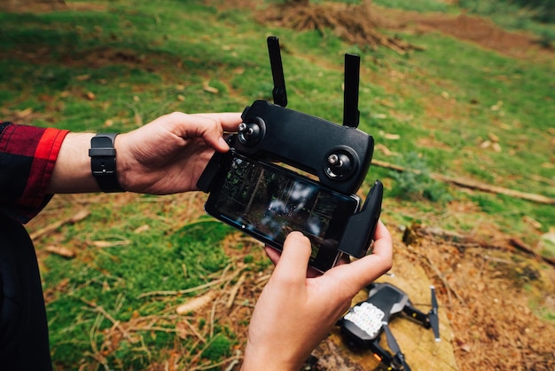 Mains d'un jeune homme sur une télécommande pour contrôler un drone sur fond de mousse dans les bois