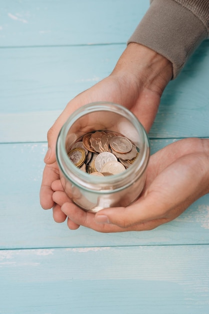 Mains de jeune homme tenant un bocal en verre avec de l'argent (pièces de monnaie) à l'intérieur