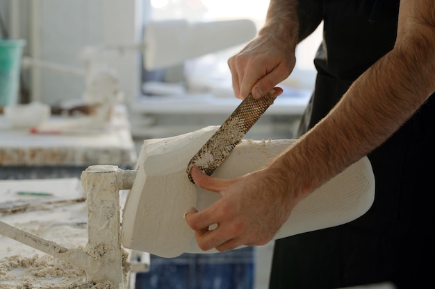 Mains d'un jeune ouvrier d'usine enlevant un excès de plâtre de la surface du plâtre