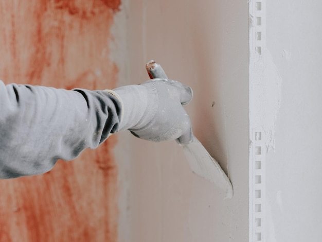 Photo les mains d'un jeune plâtrier caucasien dans des gants de construction appliquent du mastic frais sur le mur