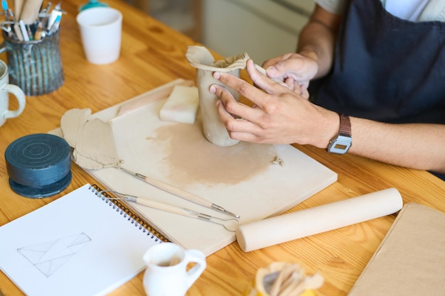 Photo mains de jeune potier mâle formant la forme d'un vase ou d'une cruche par son lieu de travail