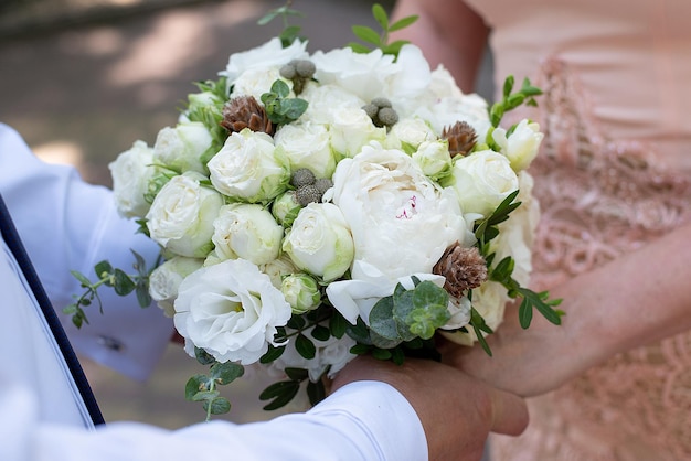 Mains des jeunes mariés en gros plan sur le fond du concept de bouquet de mariage pour les agences