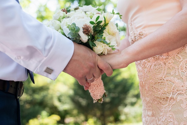 Mains des jeunes mariés en gros plan sur le fond du concept de bouquet de mariage pour les agences