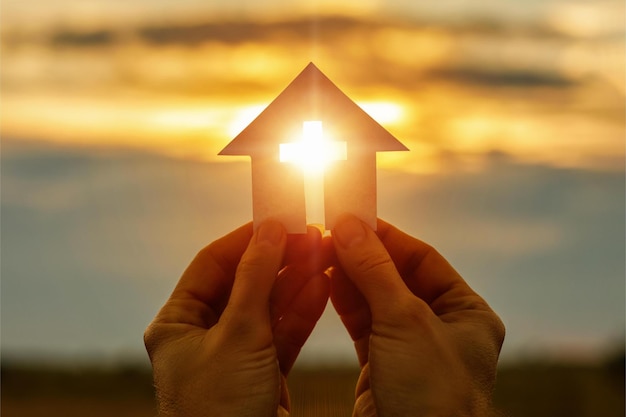 Mains avec maison de prière en papier dans les mains contre le ciel