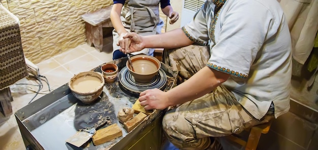 Les mains d'un maître et d'un étudiant fabriquent un pichet sur une roue de potiers en argile jaune Mise au point sélective sur les mains