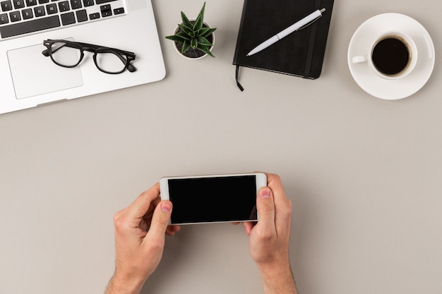 Mains mâles à l'aide de smartphone blanc en orientation paysage sur un bureau moderne gris