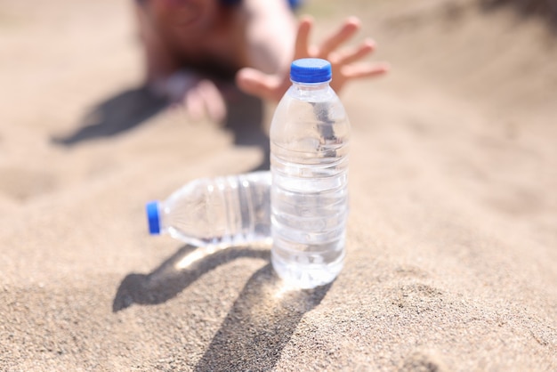 Mains mâles atteignant une bouteille d'eau en plastique dans le désert en gros plan