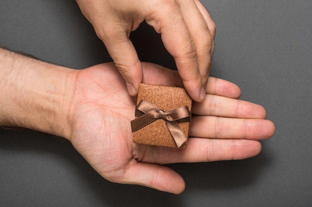 Mains mâles avec une boîte à bijoux marron. Présent. Fond noir