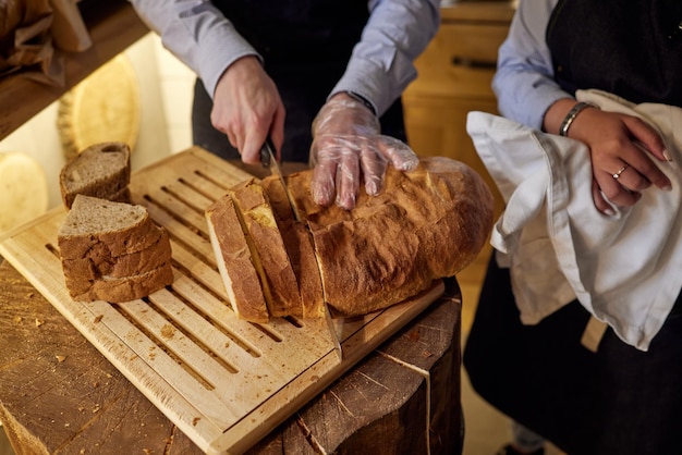 Mains mâles coupant du pain de blé sur la planche de bois, mise au point sélective.