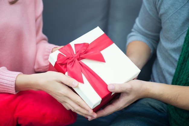 Mains mâles et femelles tenant une boîte cadeau doré avec ruban rouge. Cadeau pour anniversaire, Saint Valentin, Noël