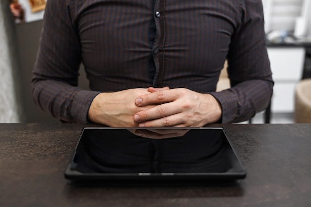 Mains mâles d'un homme d'affaires à côté d'une tablette noire avec un écran vide sur la table